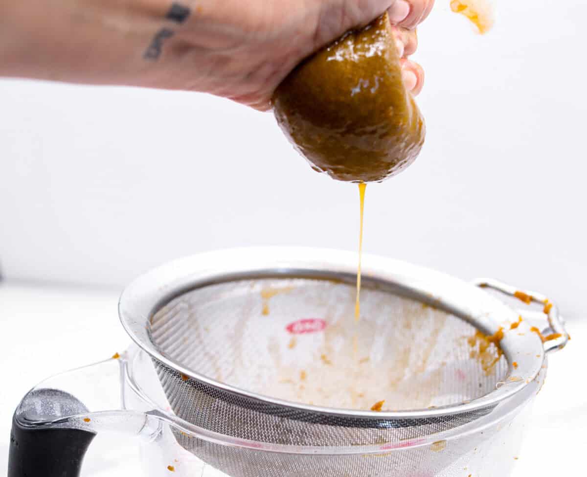 Side shot of someone holding the cheesecloth with pumpkin puree mixture squeezing the juice out. 