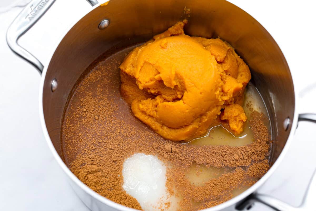 Overhead shot of pumpkin puree, water, sugar and spices in a sauce pan. 