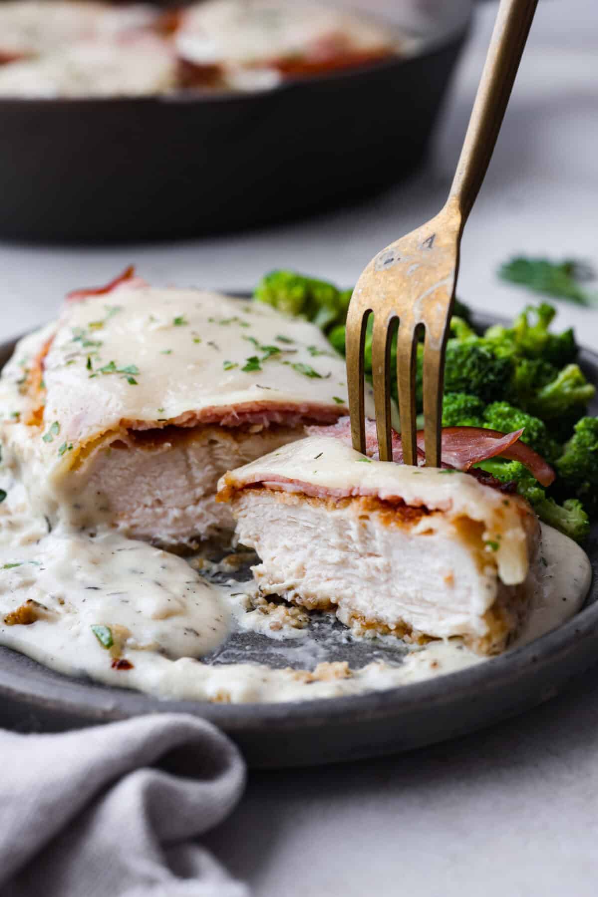 Side shot of plated chicken cordon blue cut in half with a fork sticking out of a bite. 