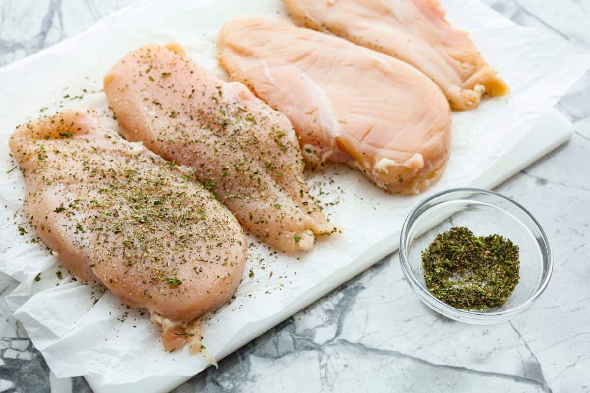 Angle shot of chicken breasts being coated in seasonings. 