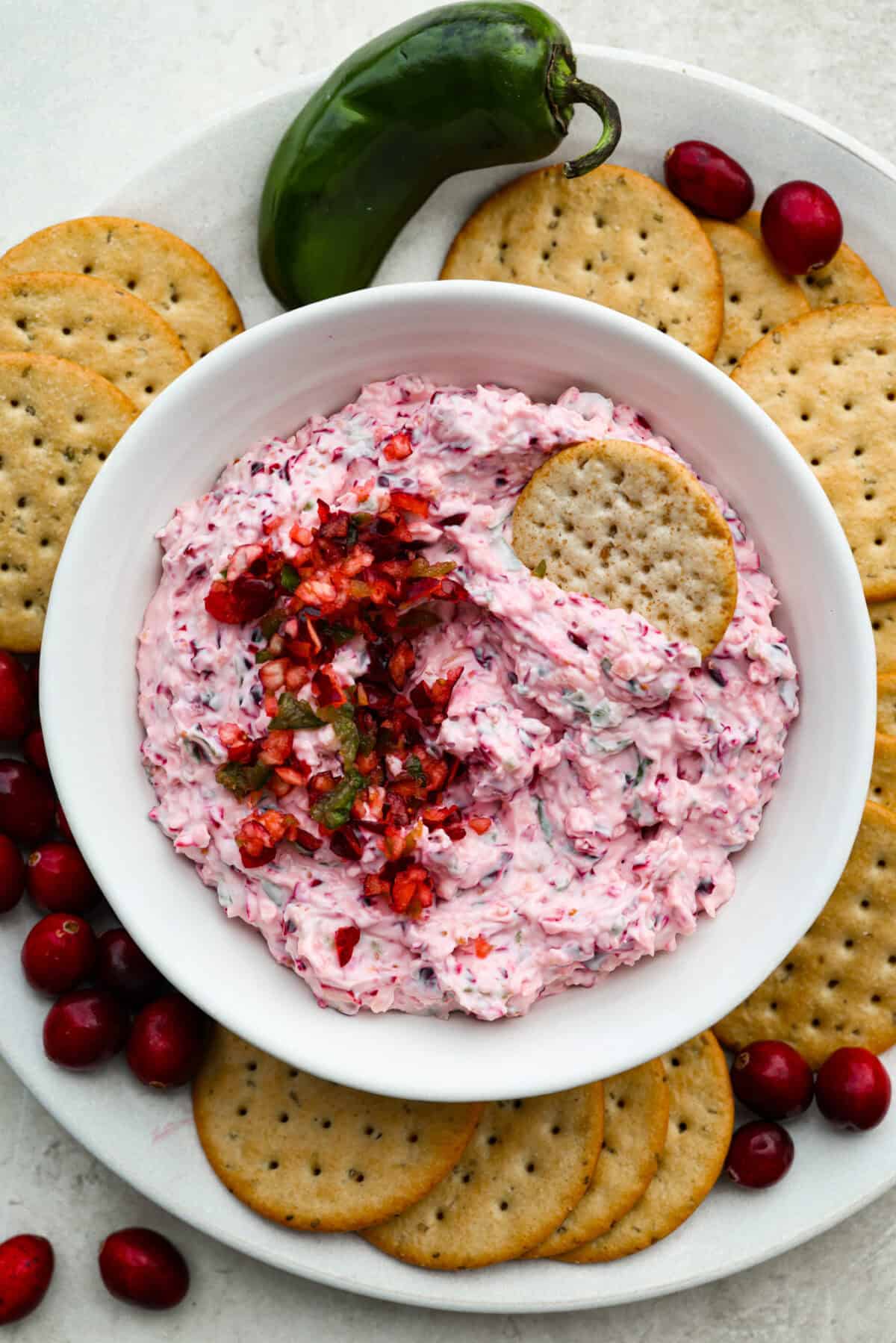 Bowl of cranberry jalapeño dip surrounded by crackers, cranberries and jalapeños.