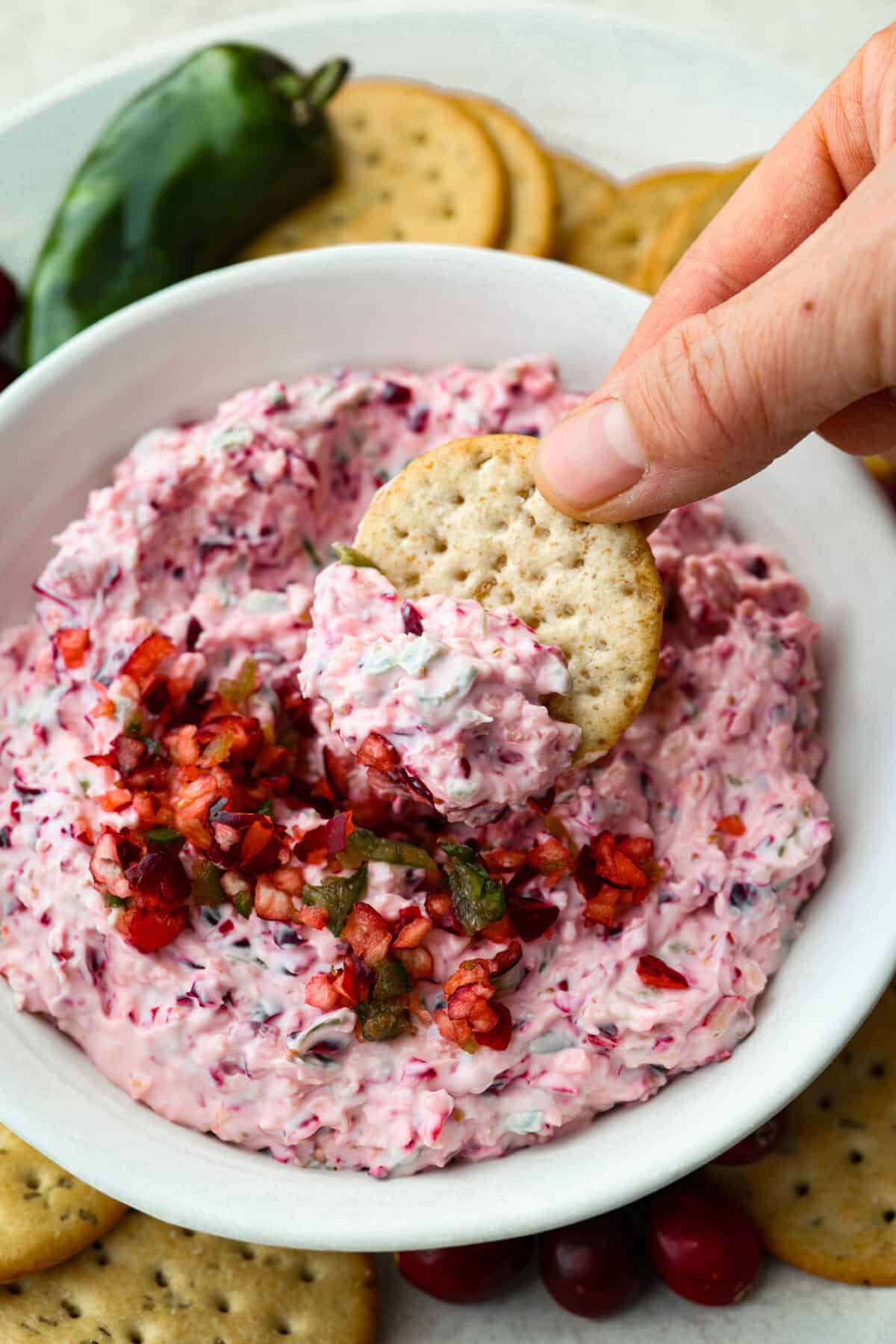 Someone scooping a bite of the cranberry jalapeño dip with a cracker. 