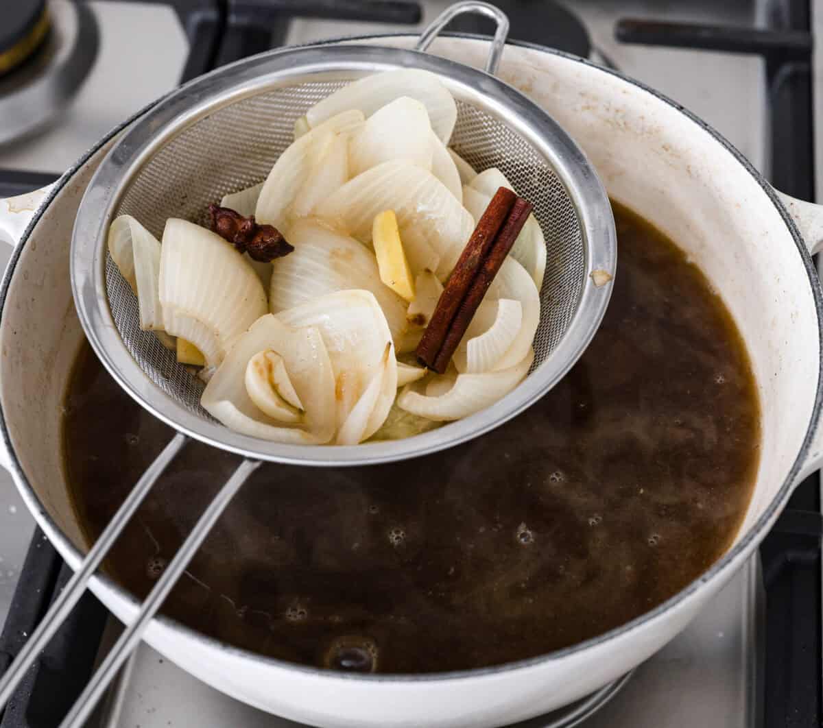 Angle shot of someone lifting the onions and seasonings out of the broth. 