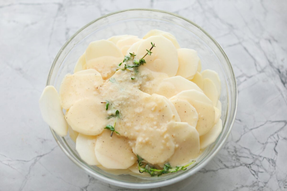Thinly sliced potatoes in a bowl covered in butter mixture. 