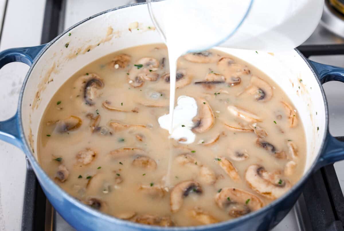 Angle shot of cream being poured into the mushroom, flour and broth mixture. 