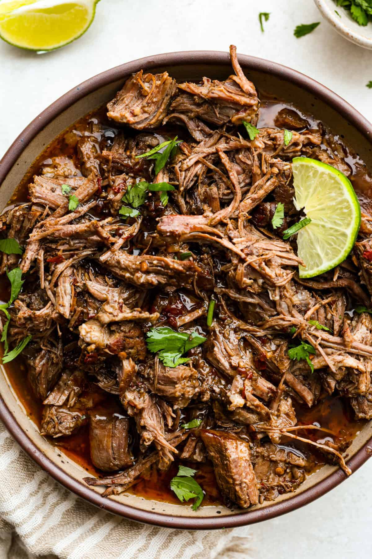 Bowl of slow cooker Barbacoa beef garnished with cilantro and lime. 