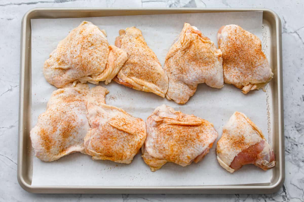 Seasoned chicken thighs on a piece of parchment paper lined baking sheet. 
