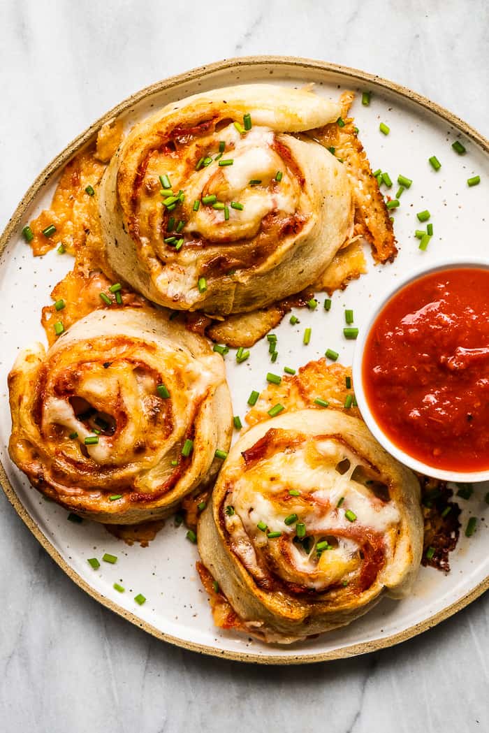 A white plate with pizza pinwheels and a red dipping sauce.