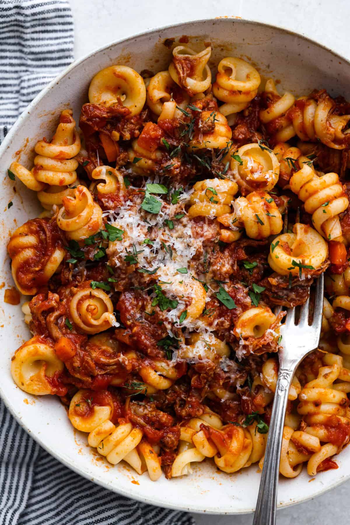 Overhead shot of plated slow cooker Sunday sauce with pasta and garnished with parmesan cheese. 