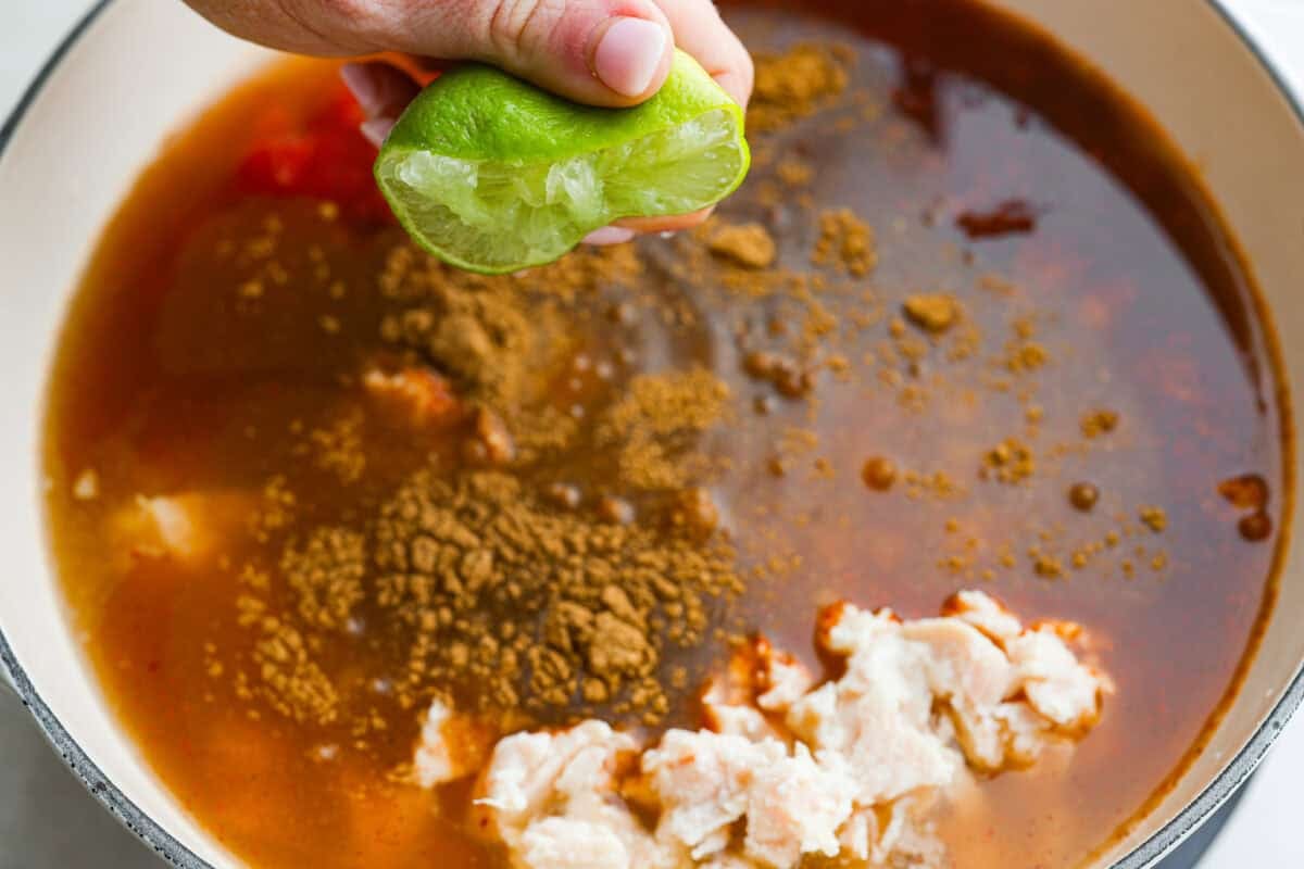 Someone squeezing lime juice over the seasoned canned ingredients in the pot.