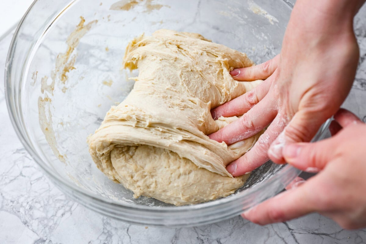 Someone pulling and smashing one side of the dough ball over the whole dough ball.