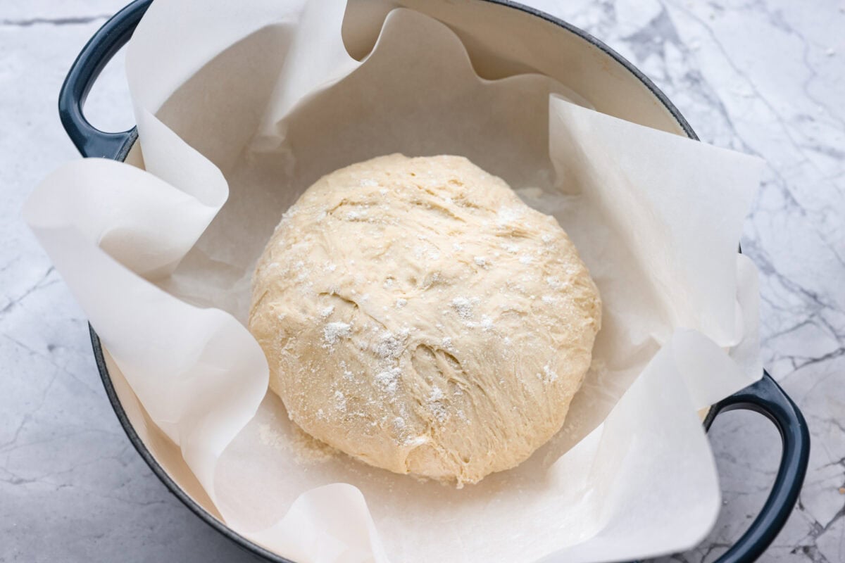 Ball of dough floured and placed in a dutch oven with parchment paper.