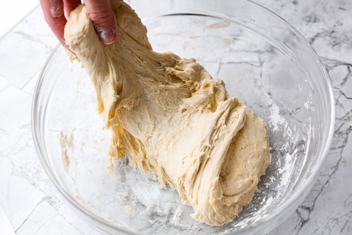 Someone stretching another side of the dough ball ready to fold it over the whole dough ball. 