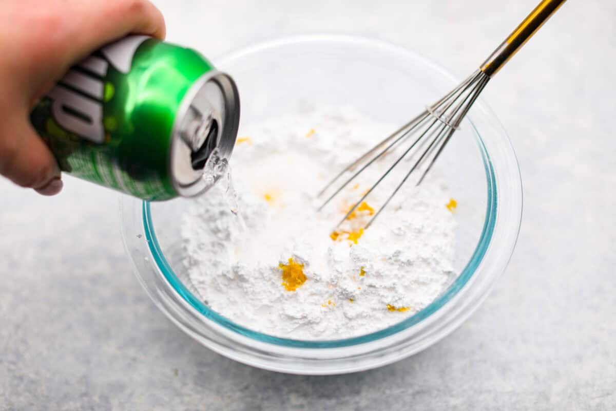 Someone pouring 7Up into the lemon zest and powdered sugar mixture to make the glaze. 