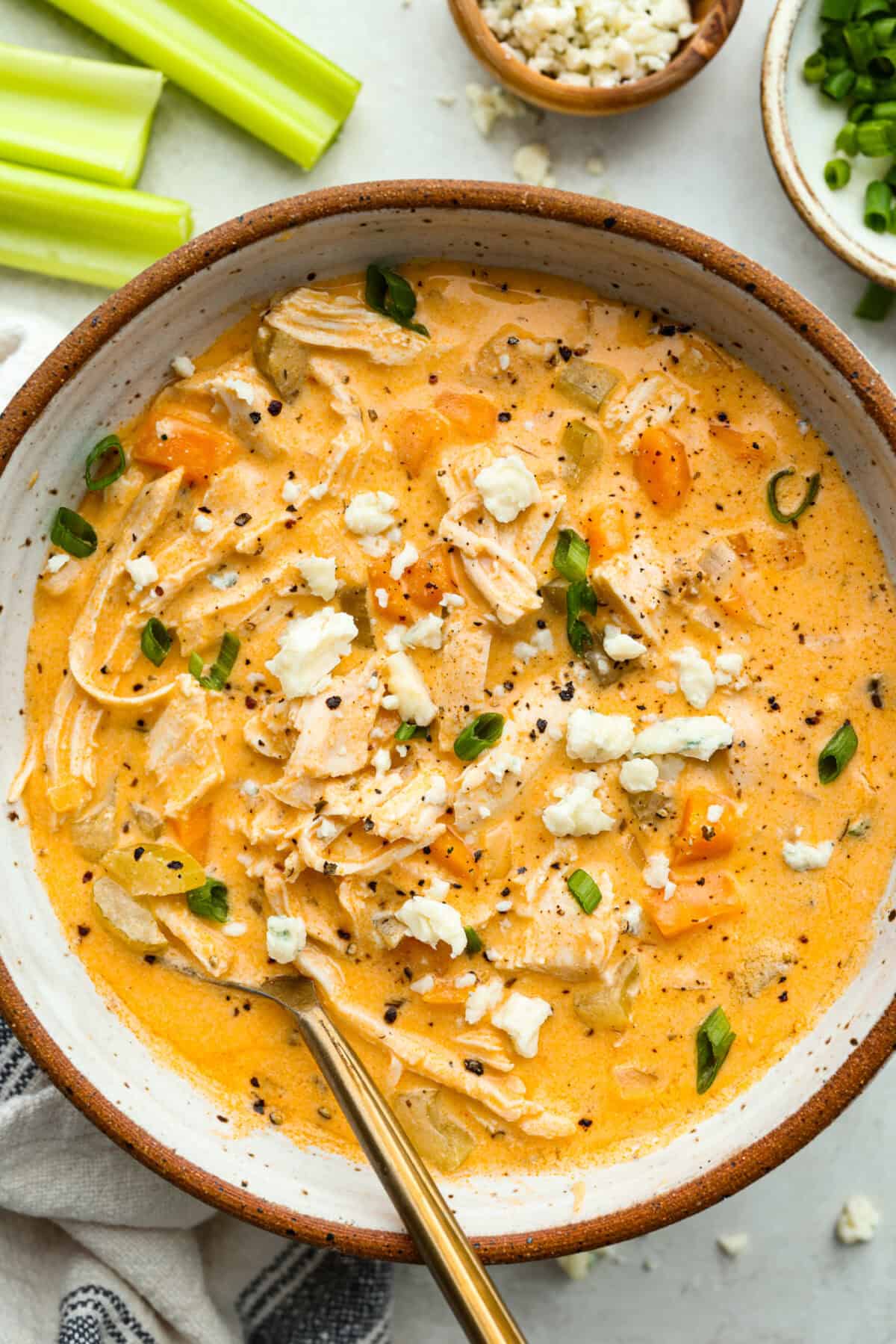 Overhead shot of a bowl of buffalo chicken soup garnished with blue cheese crumbles and green onions. 
