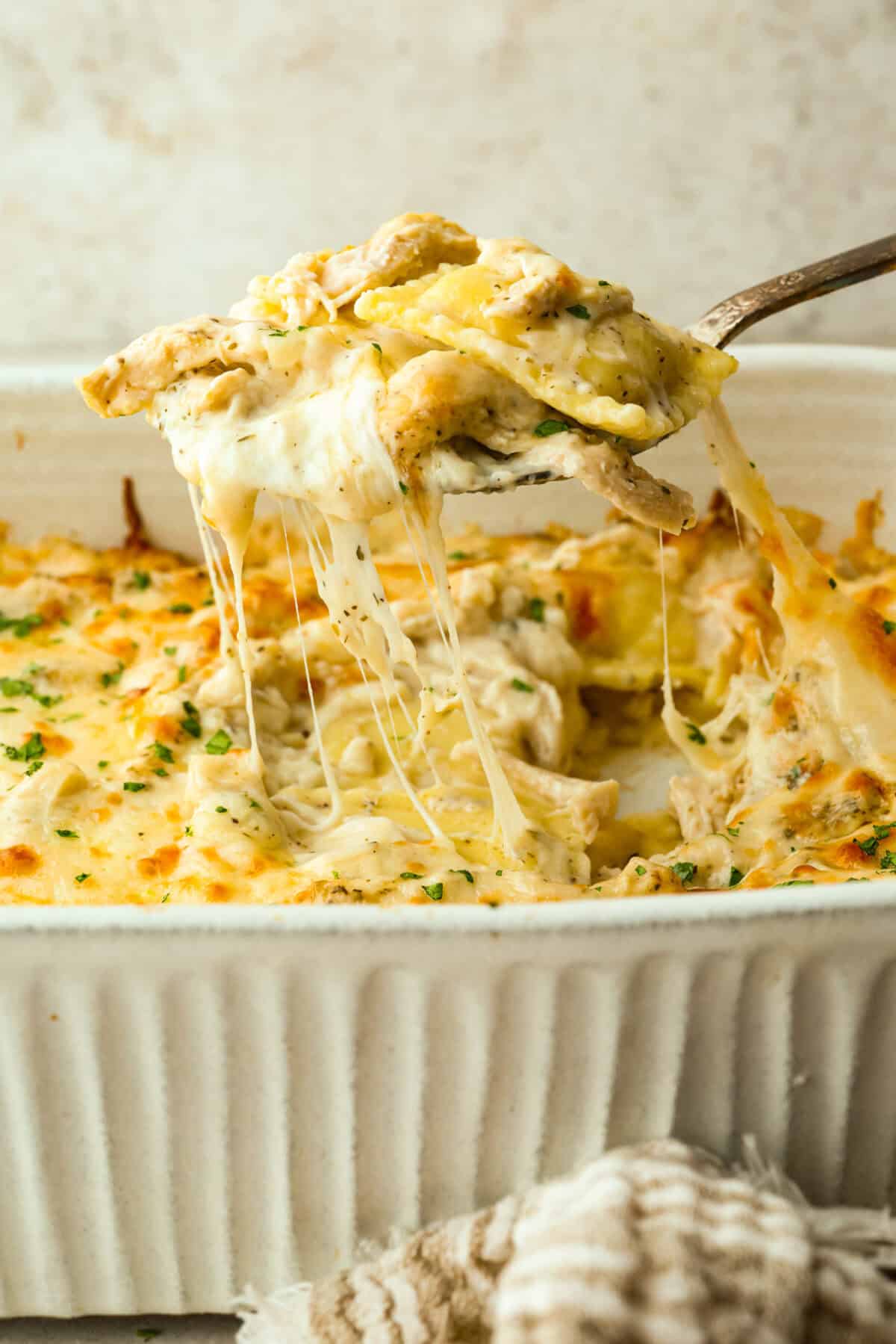 Someone scooping a portion of alfredo ravioli casserole from the baking dish. 