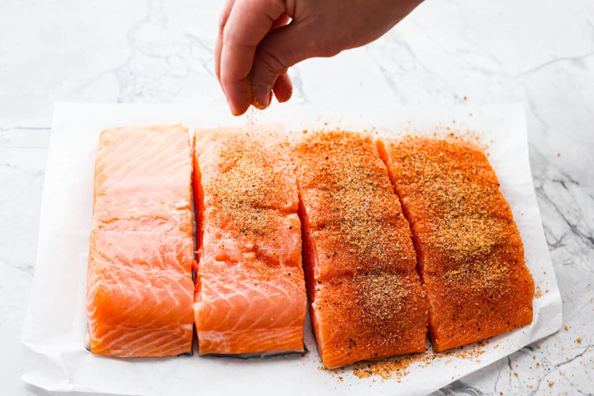 Someone sprinkling spice rub over the salmon filets. 
