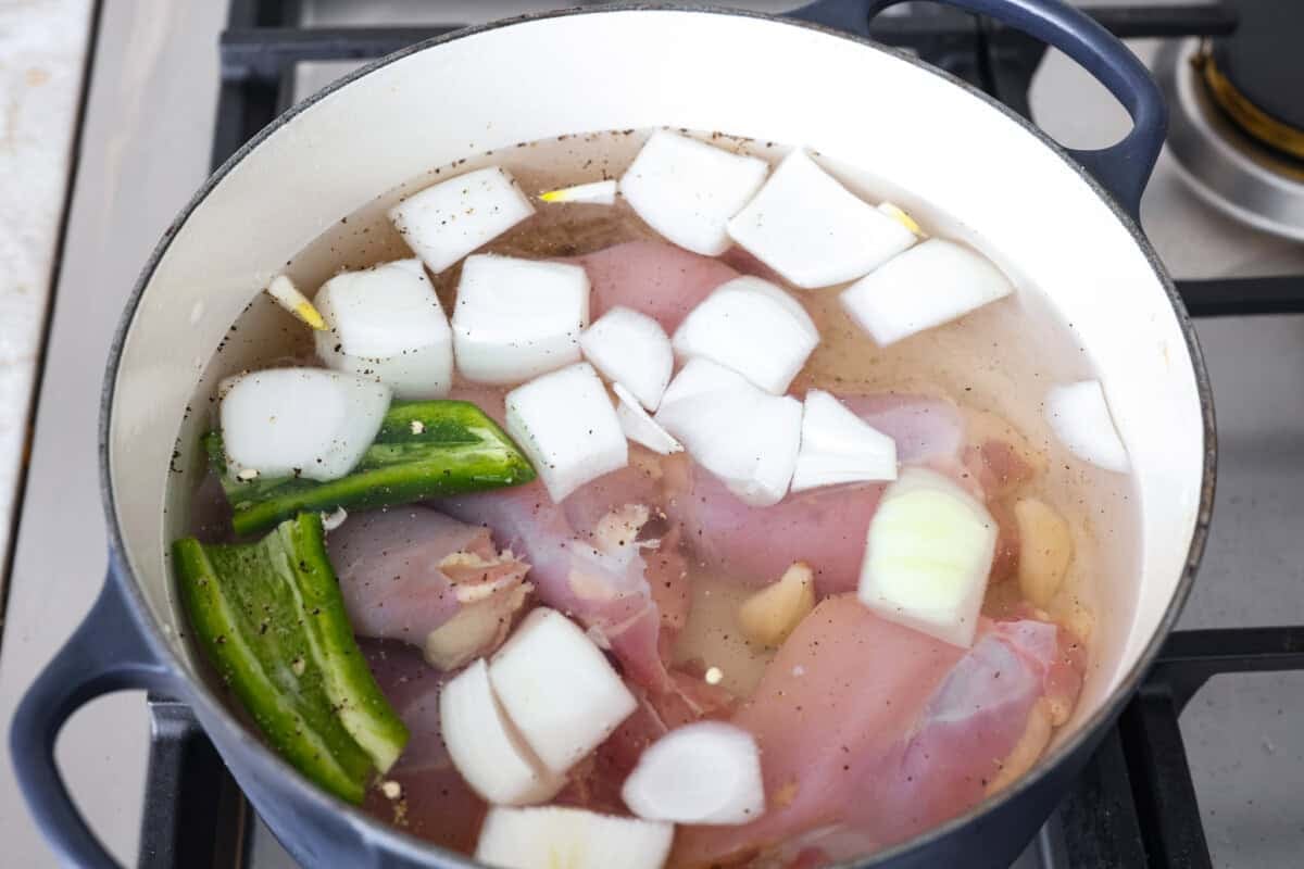 Overhead shot of a large pot with the water, chicken, onions, jalapeno, garlic, salt and pepper added. 