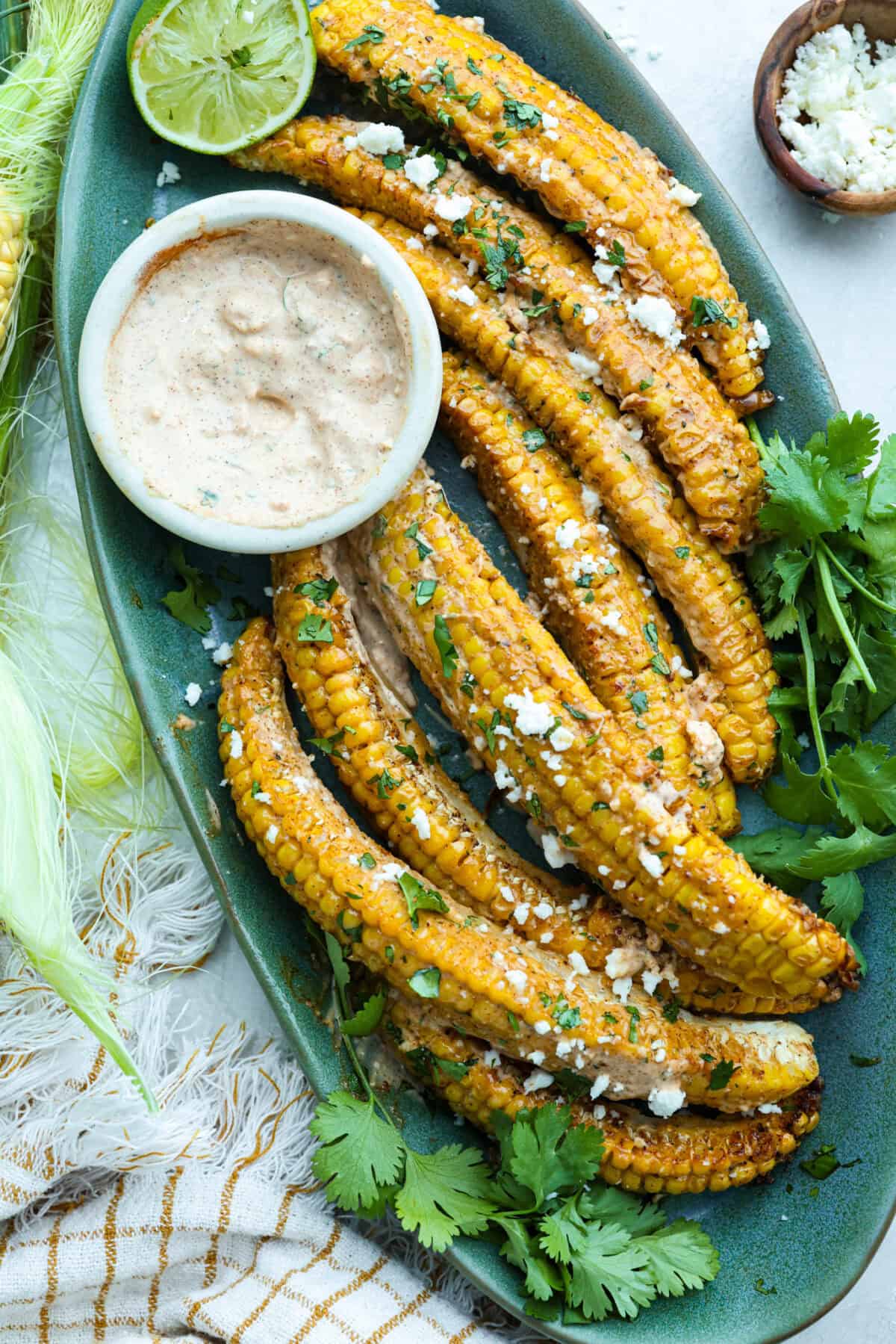 Serving platter with cooked corn ribs smothered in Eloté sauce and garnished with Cotija cheese and cilantro. 