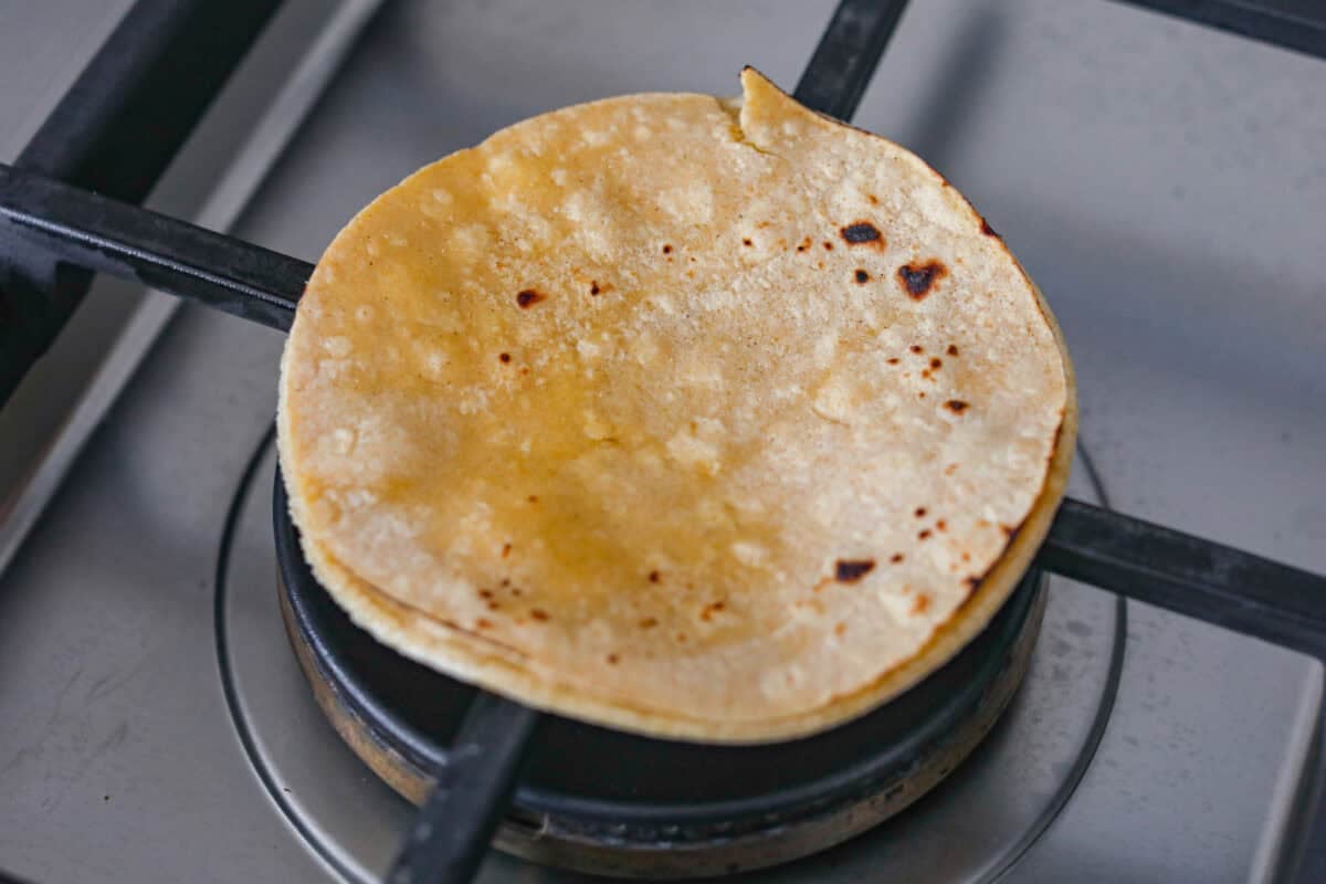Corn tortillas being cooked on a gas burner. 