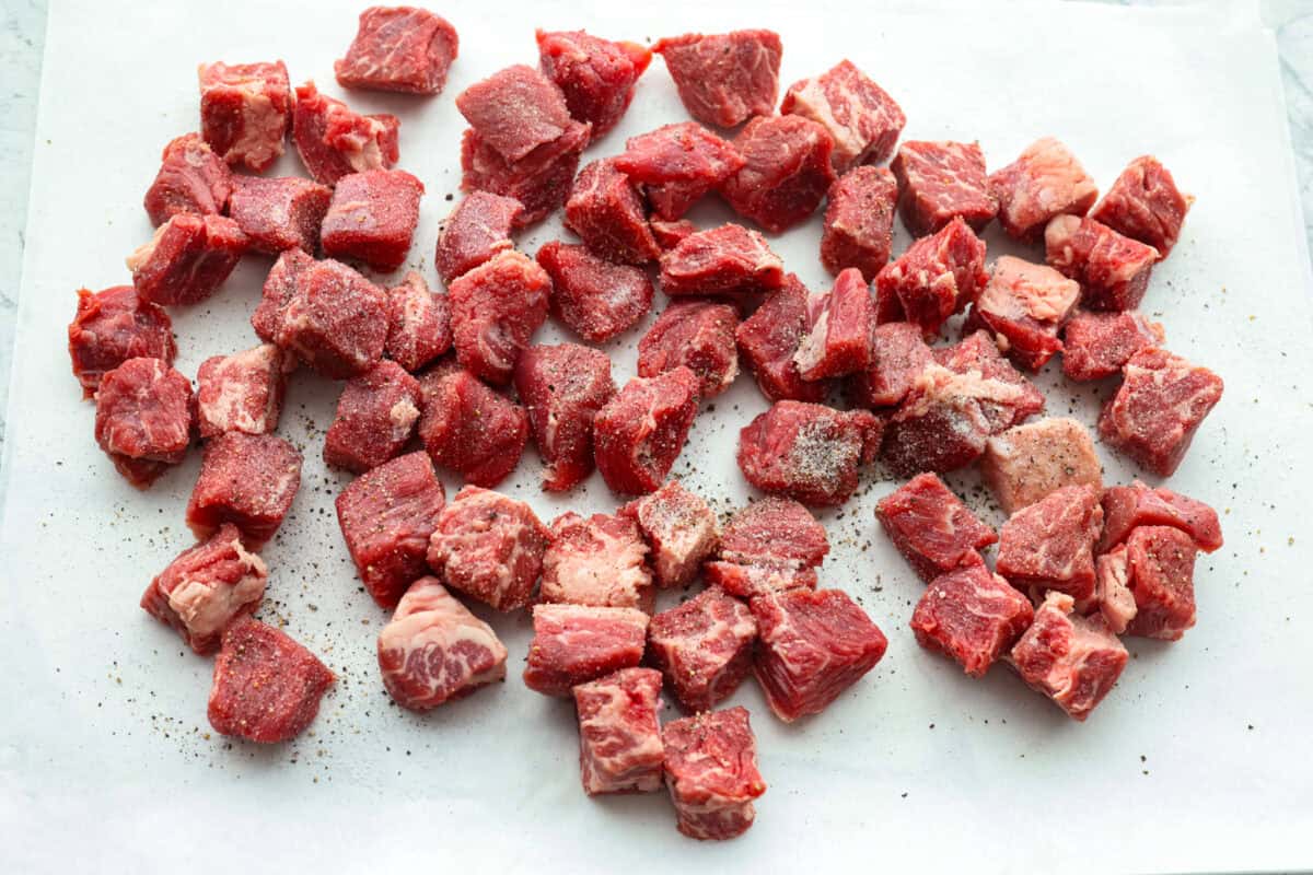 Chuck roast cute into cubes and seasoned on a cutting board. 