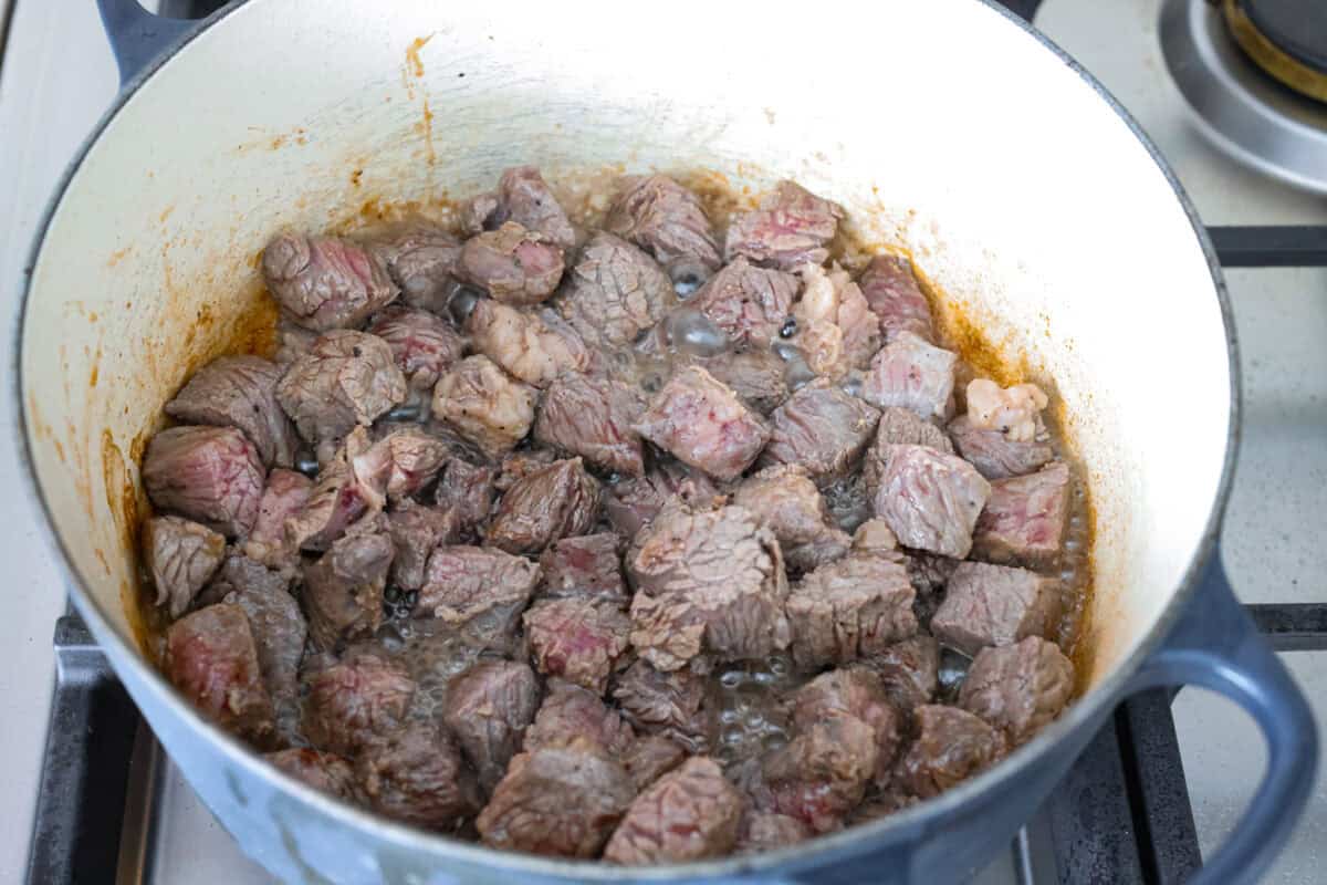 Browning the beef at the bottom of a dutch oven on the stove top.