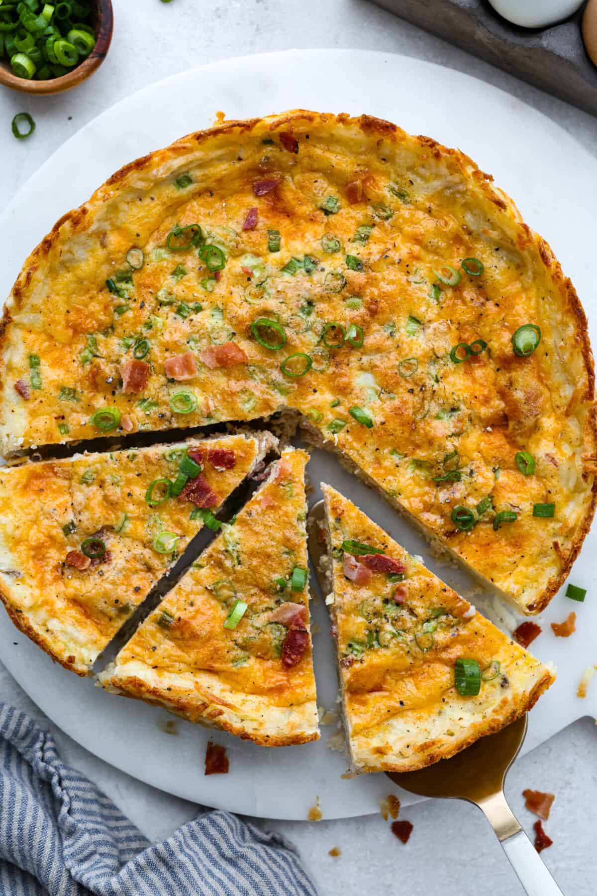 Top down shot of hash brown crust quiche on a serving platter with a few slices a little bit separated. 