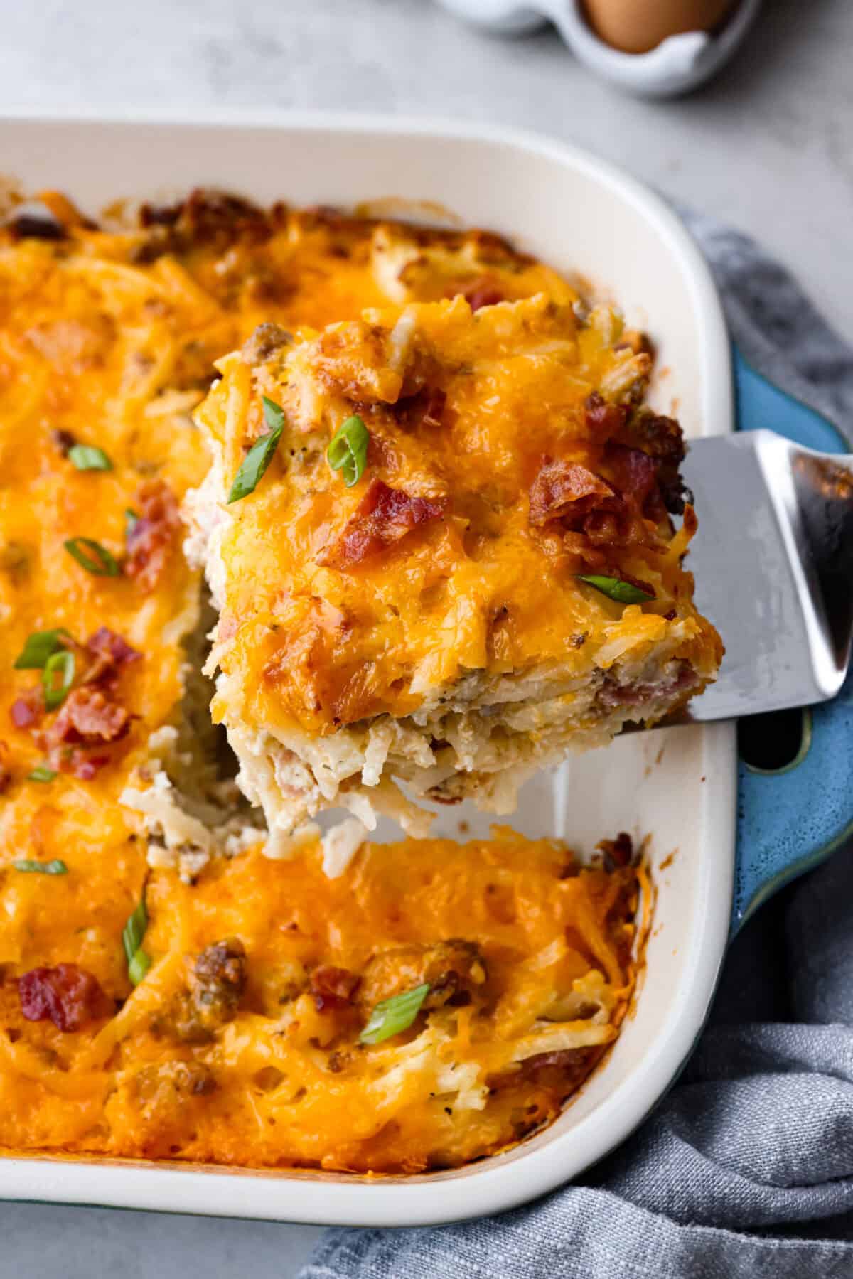 Angle shot of a serving of crack breakfast casserole being lifted out of the baking dish with a spatula. 