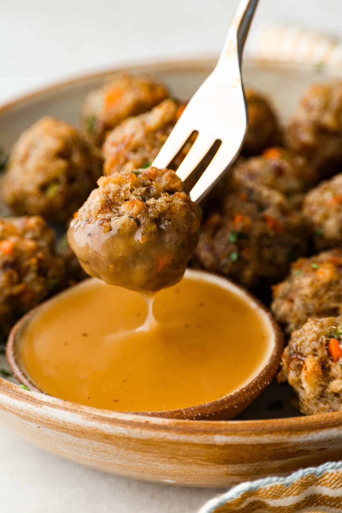 Someone dipping a sausage ball into some gravy. 