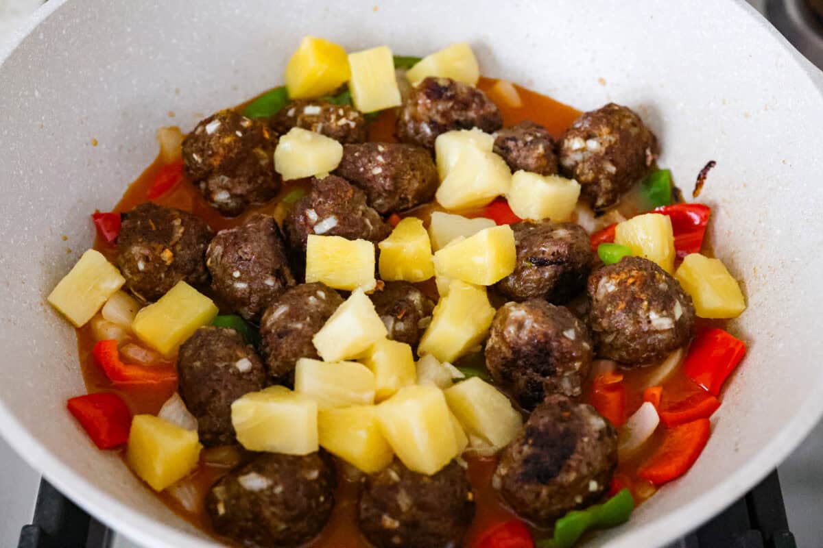 Meatballs, veggies, and pineapple all doused in the sauce and cooking in a skillet. 