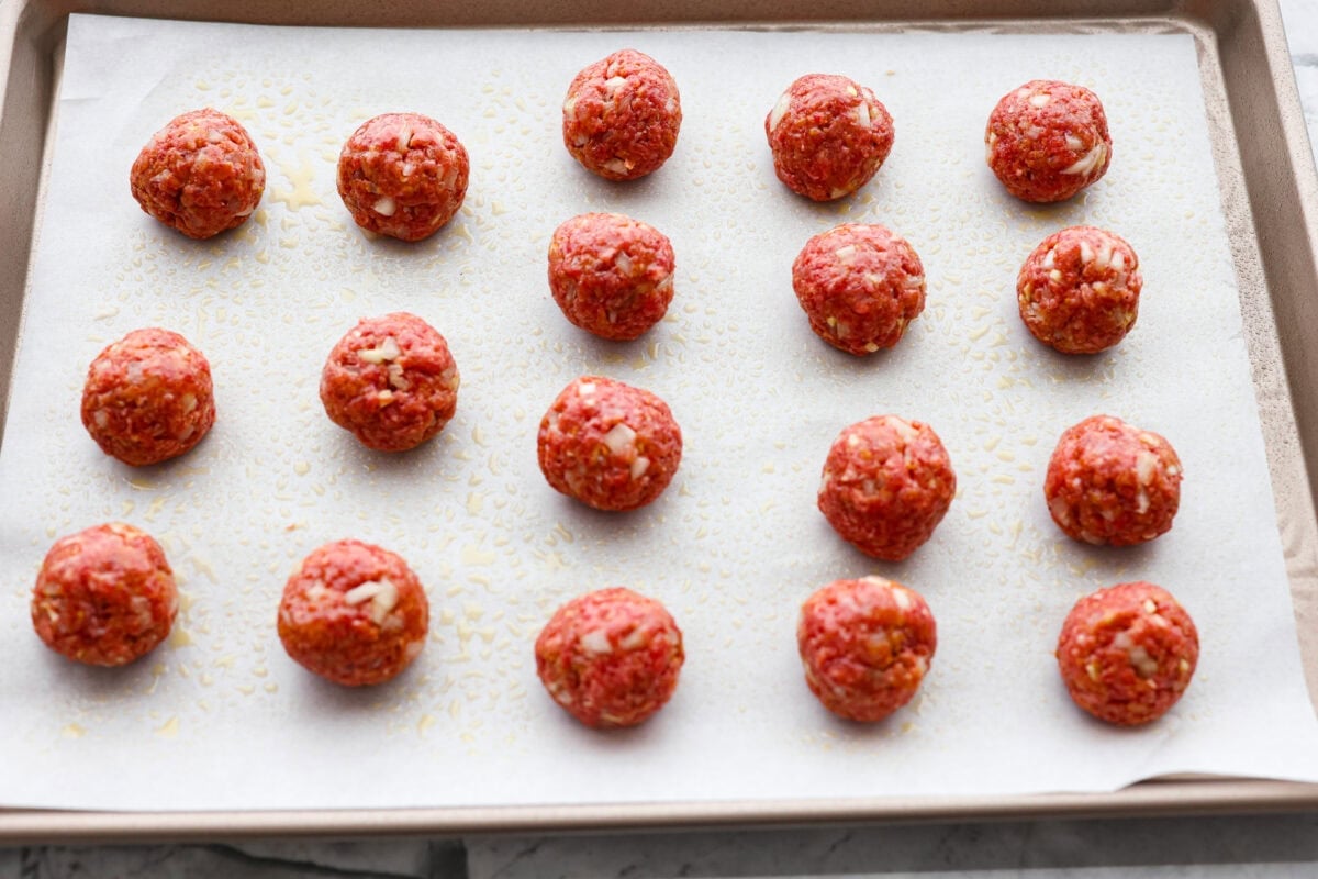 Meatballs mixed and formed into balls on a parchment lined cookie sheet.