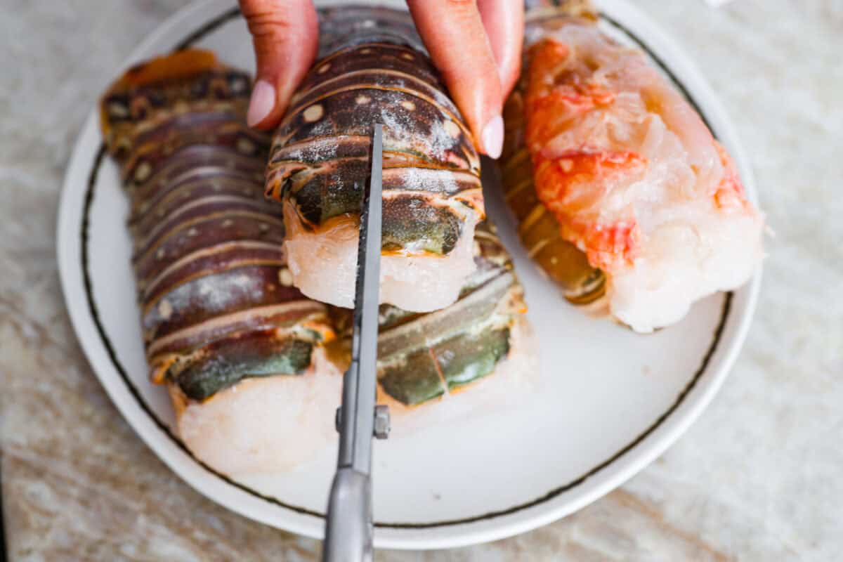 Someone cutting the shell on the top of the lobster tail with kitchen sheers.