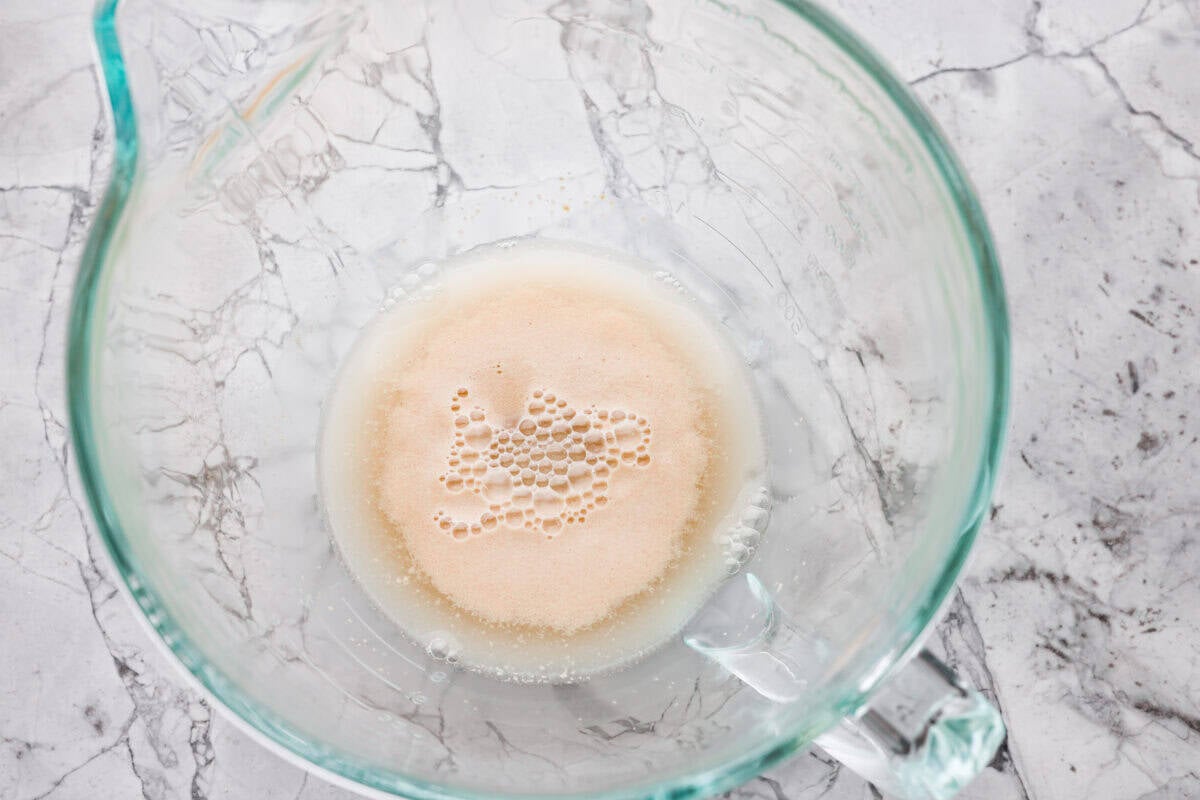 Water, sugar, and yeast added to a stand mixer bowl. 