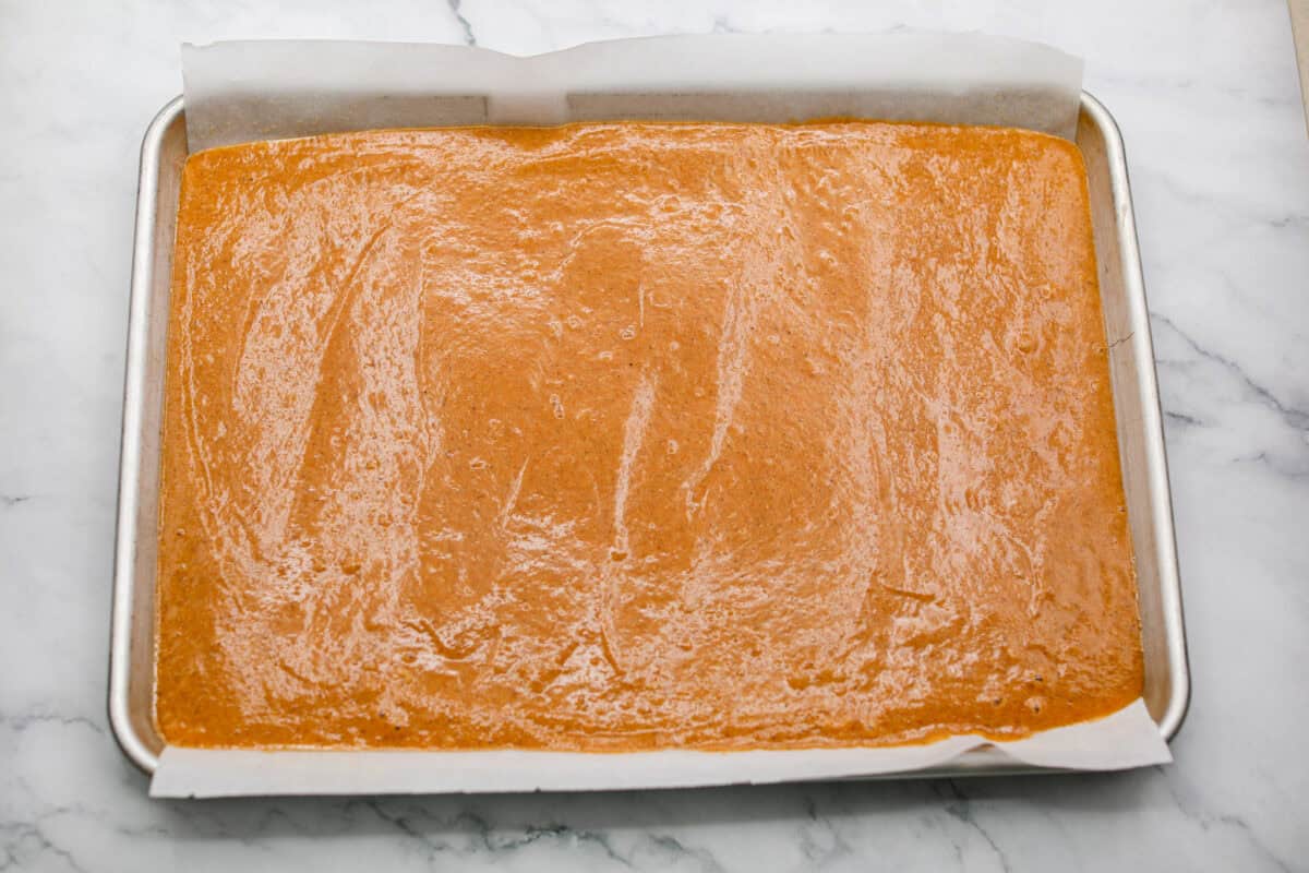 Cake batter spread out on the parchment paper on a jelly roll pan.