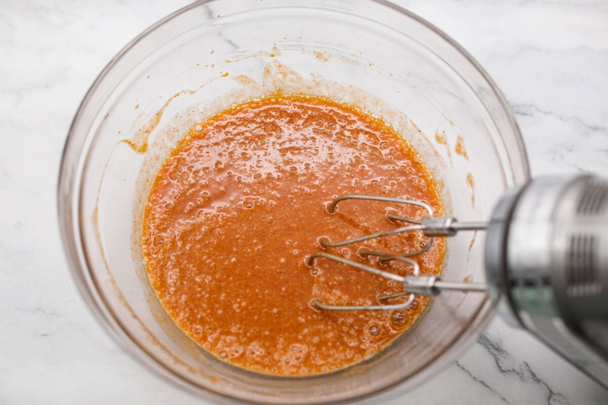 Someone using a hand mixer to beat together eggs, sugar, pumpkin, vanilla, cinnamon, and cloves. 