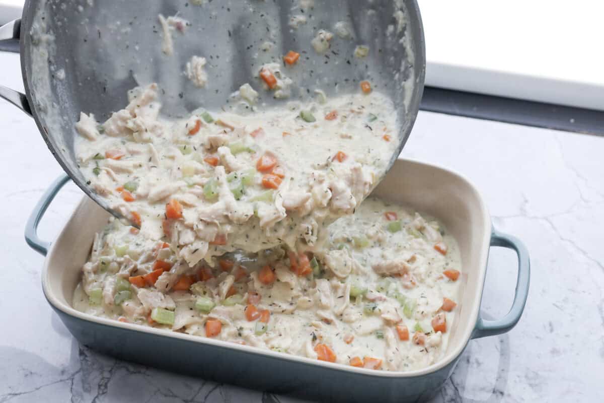 Angle shot of someone pouring the veggie, chicken and sauce mixture into a baking dish. 