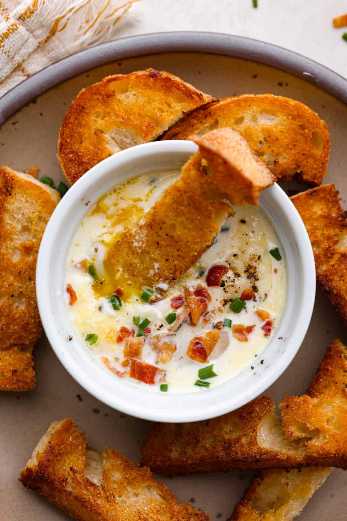 Overhead shot of shirred eggs in a ramekin surrounded by crostini.