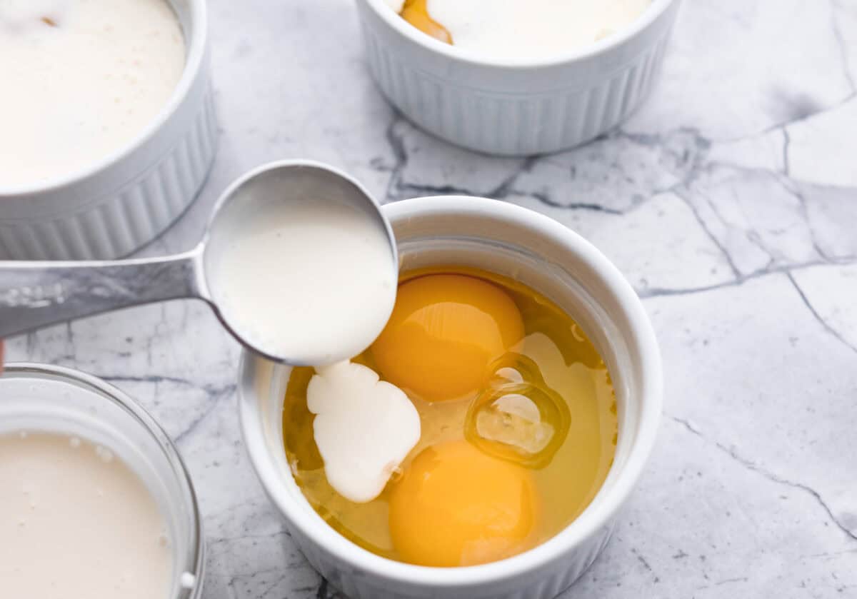 Overhead shot of ramekin with two eggs and someone pouring cream in it.