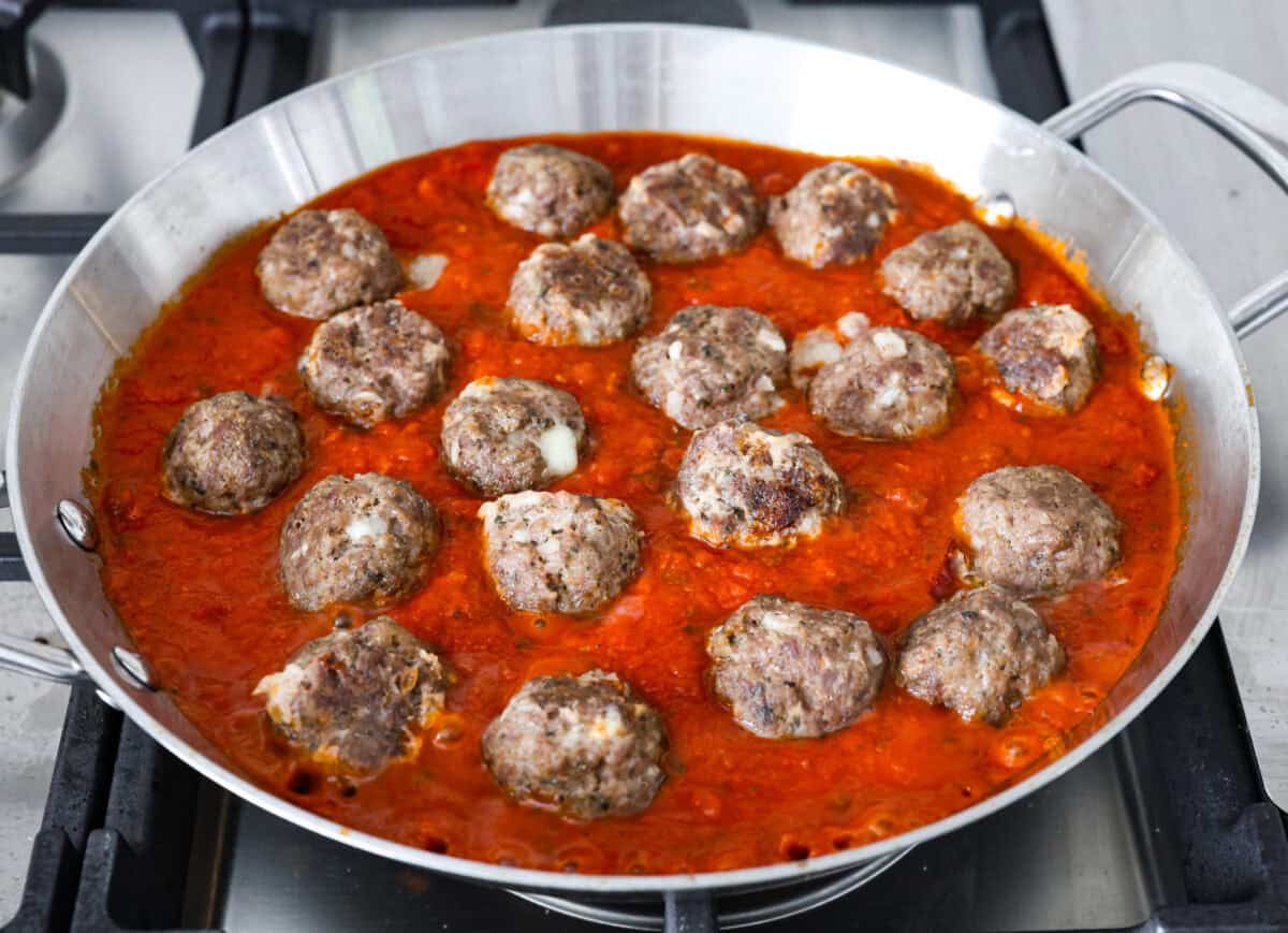 Sixth photo of the mozzarella stuffed meatballs placed in a pan of marinara sauce.