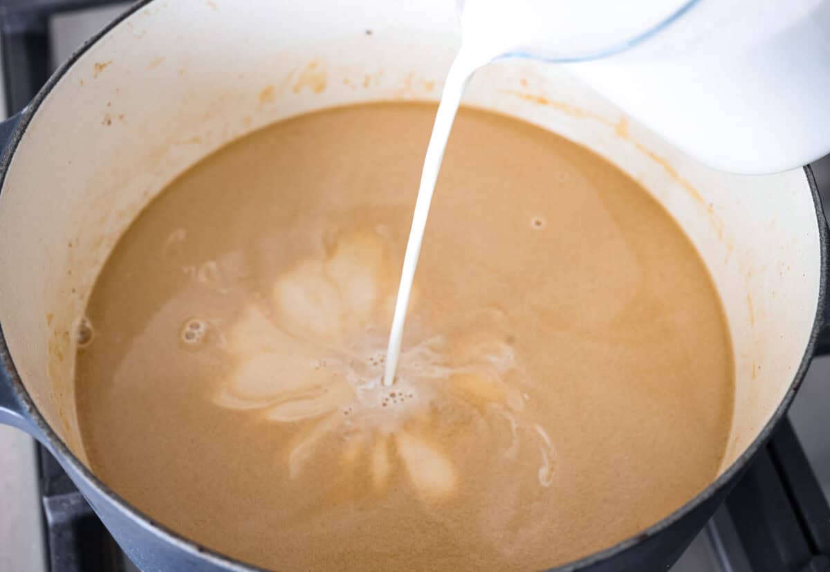 Angle shot of someone pouring half and half into the beef broth and onion mixture. 