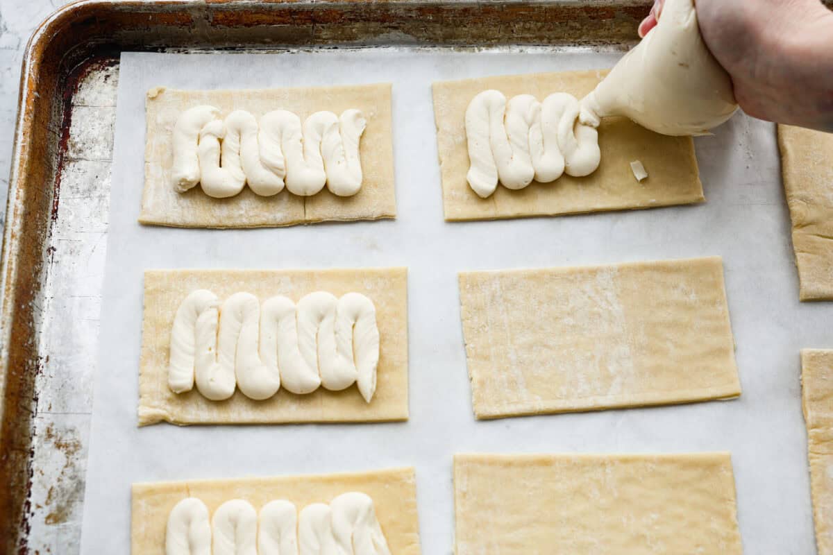 Overhead shot of someone piping the cream cheese filling onto the rectangle puff pastry. 