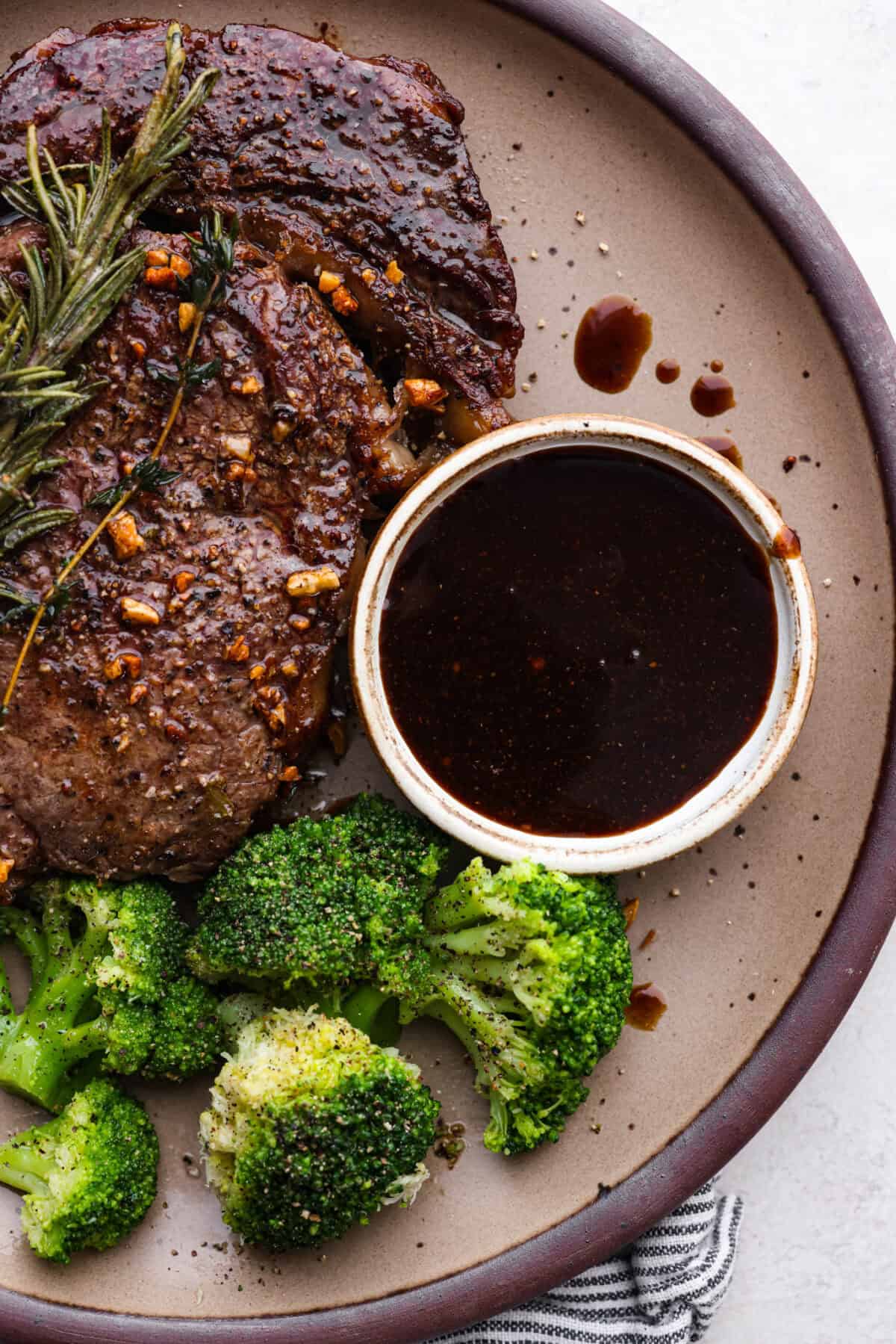 Overhead shot of a plate with steak next to broccoli, and a small bowl of homemade steak sauce. 