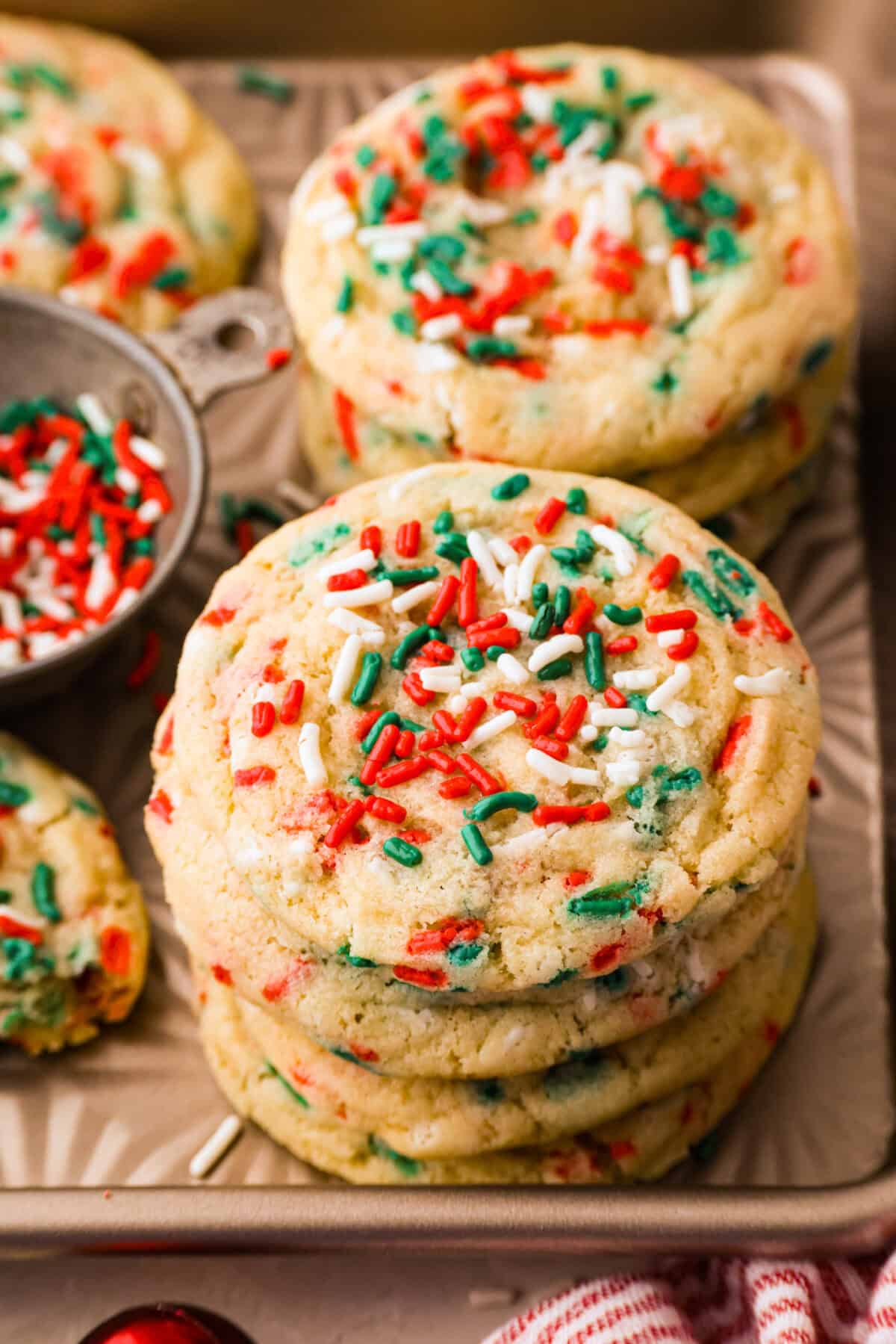 Close up angle shot of a stack of Christmas sprinkle cookies next to a bowl of sprinkles. 