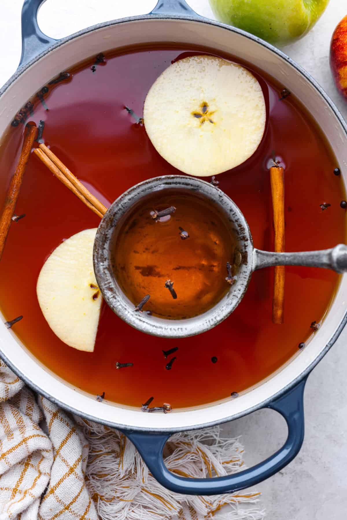 Overhead shot of mulled cider with apple slices, cinnamon sticks cloves and allspice berries in a pot.