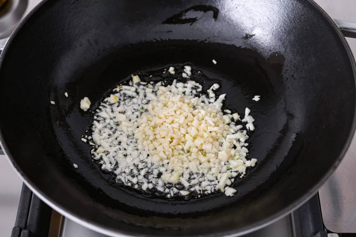 Angle shot of minced garlic added to oil in a wok. 