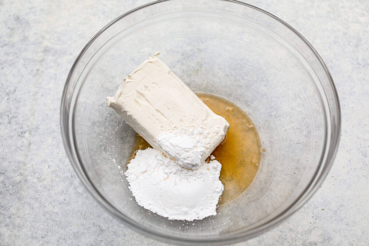 Overhead shot of cream cheese, extracts and powdered sugar in a bowl. 