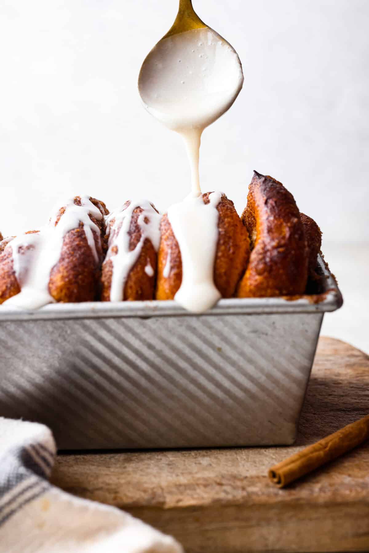 Side shot of glaze being drizzled over the cinnamon pull-apart bread. 