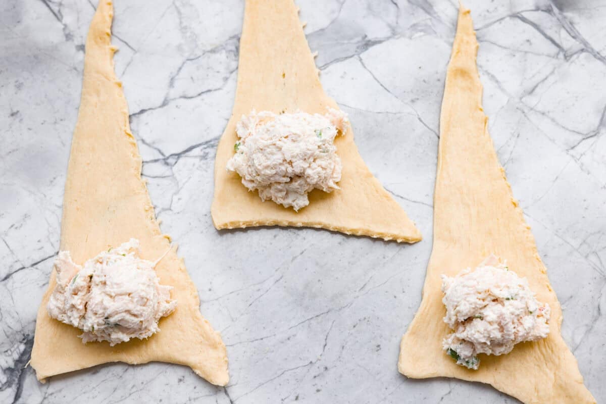 Crescent roll triangles separated and spread out with a dollop of chicken mixture scooped onto the wide end. 