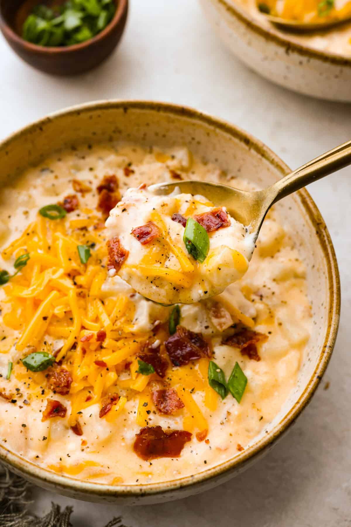 Close up shot of crock pot crack potato soup on a spoon over bowl. 