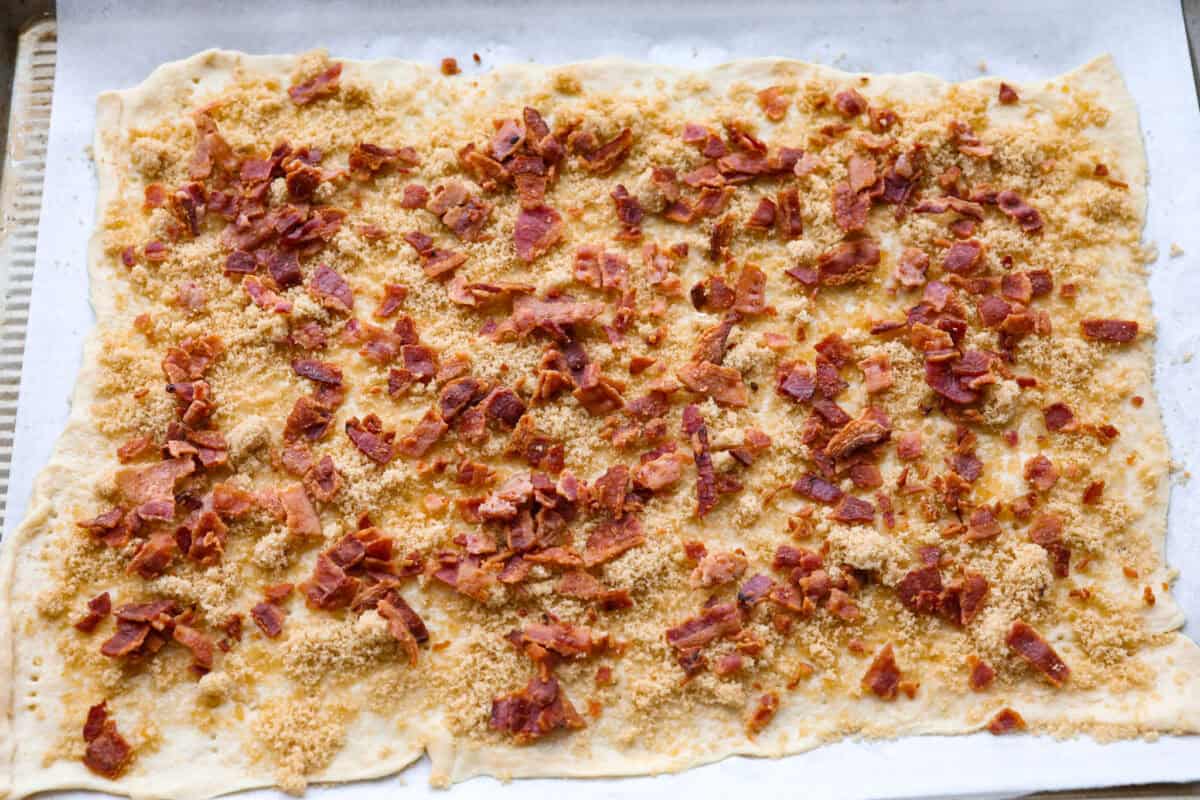 Overhead shot of bacon pieces over the brown sugar and maple on the crescent dough. 